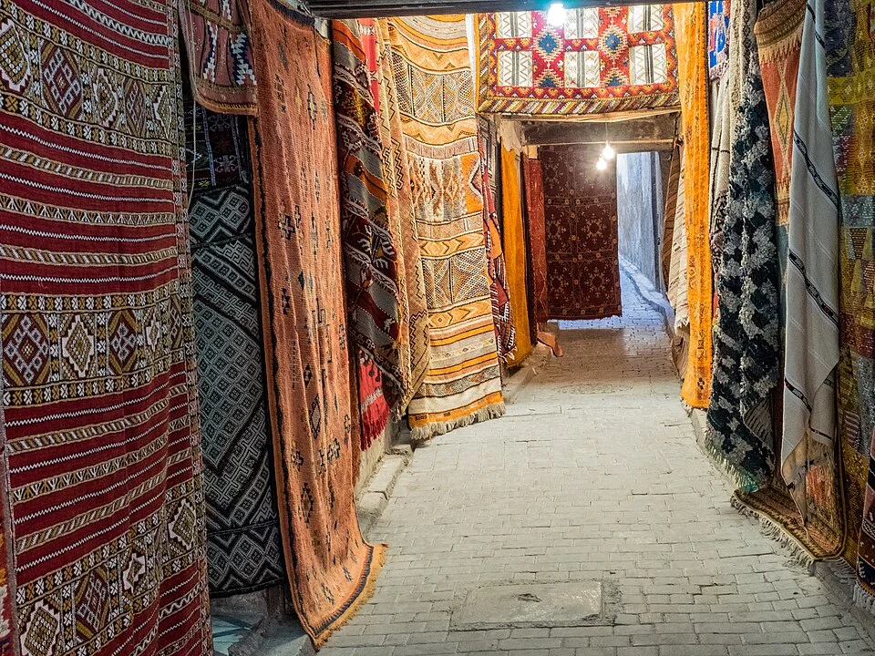 Rugs stacked in a Moroccan souk, where a serious buy still begins over a cup of tea